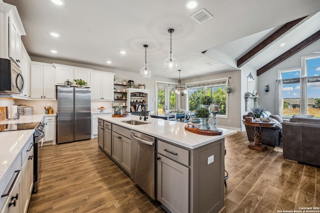 kitchen with lofted ceiling with beams, stainless steel appliances, a wealth of natural light, white cabinets, and a kitchen island with sink