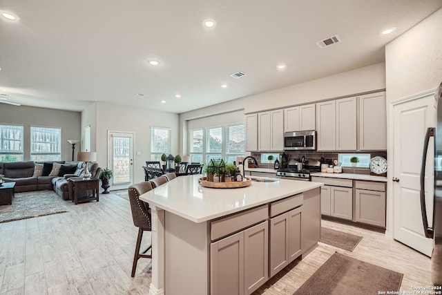 kitchen featuring a center island with sink, sink, stainless steel appliances, and gray cabinets