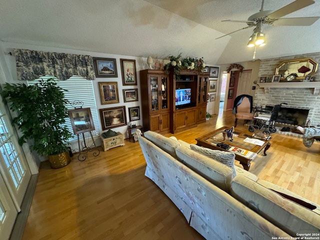 living room with wood-type flooring, a brick fireplace, ceiling fan, and lofted ceiling