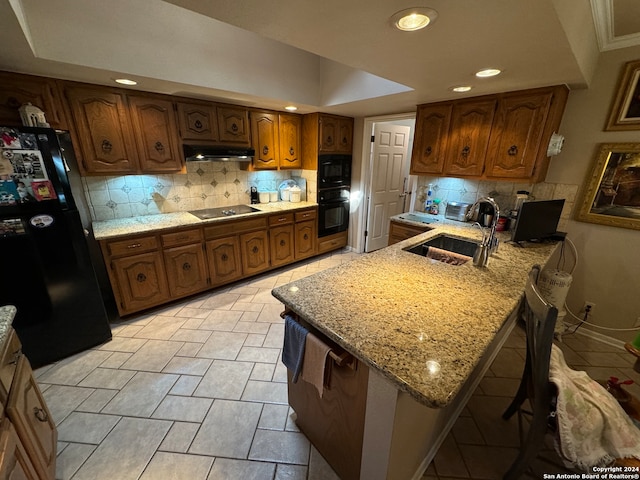 kitchen with a breakfast bar, black appliances, sink, decorative backsplash, and light stone countertops