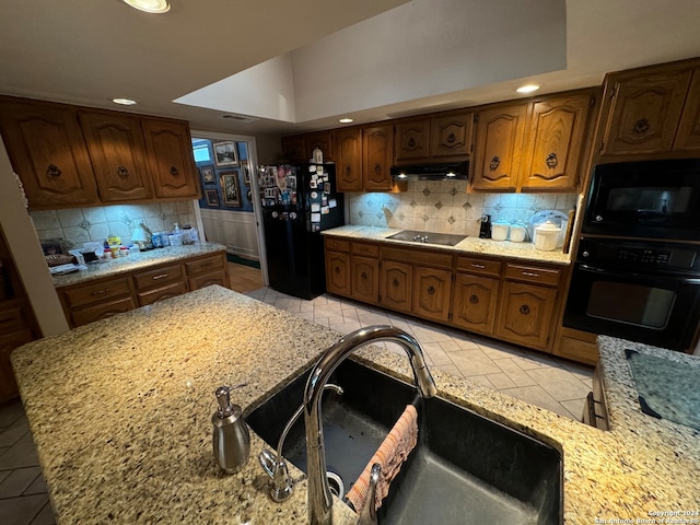 kitchen with tasteful backsplash, light stone countertops, sink, and black appliances