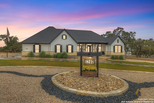 french country home featuring stone siding, a front lawn, a shingled roof, and stucco siding