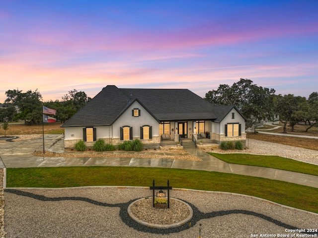 view of front of property featuring stone siding, a front lawn, roof with shingles, and stucco siding