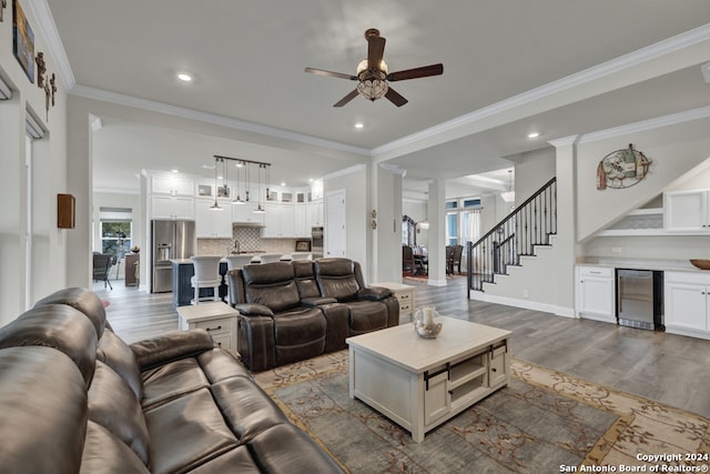 living room featuring dark wood-style floors, crown molding, ceiling fan, baseboards, and stairs