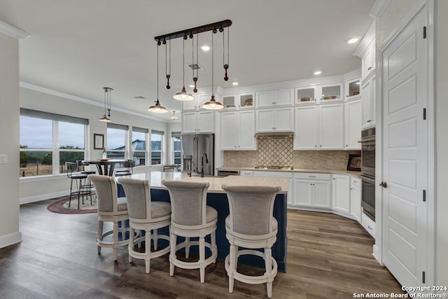 kitchen with a kitchen island with sink, stainless steel appliances, light countertops, tasteful backsplash, and glass insert cabinets