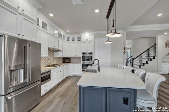 kitchen with a breakfast bar area, under cabinet range hood, a sink, visible vents, and appliances with stainless steel finishes