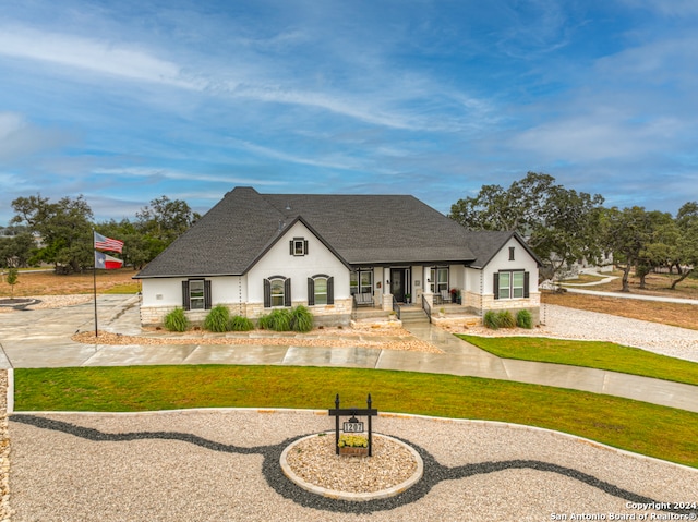 french country inspired facade featuring a shingled roof, a front yard, and stucco siding