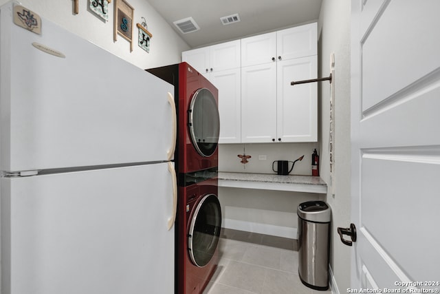 laundry room featuring visible vents, cabinet space, tile patterned flooring, and stacked washer and clothes dryer