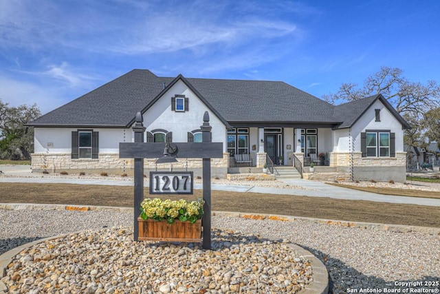 french country home featuring stone siding, stucco siding, and roof with shingles