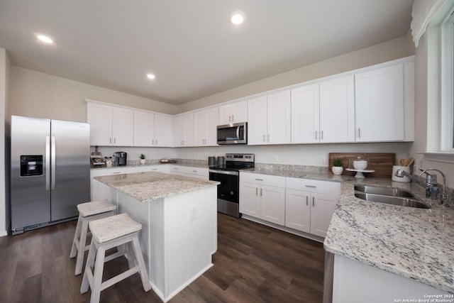 kitchen featuring dark wood-style flooring, appliances with stainless steel finishes, a sink, white cabinetry, and a kitchen island