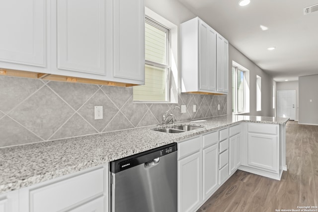 kitchen with light stone counters, white cabinetry, hardwood / wood-style flooring, stainless steel dishwasher, and sink