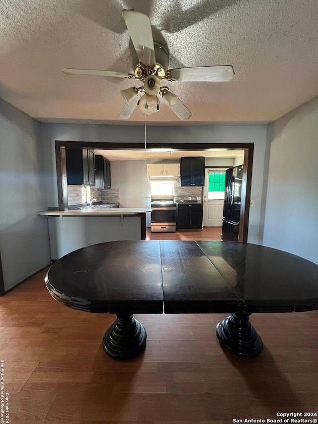 kitchen with a textured ceiling, stainless steel range oven, dark wood-type flooring, and black fridge