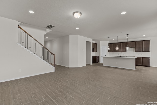 unfurnished living room with a textured ceiling, sink, and light wood-type flooring