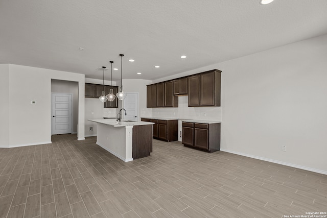 kitchen featuring light hardwood / wood-style flooring, hanging light fixtures, a center island with sink, sink, and dark brown cabinetry