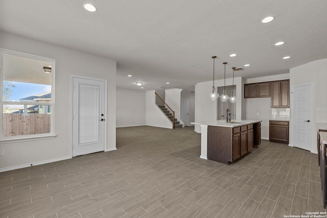 kitchen with an island with sink, sink, dark brown cabinetry, pendant lighting, and light hardwood / wood-style floors