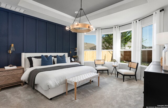 carpeted bedroom with ornamental molding, a tray ceiling, and an inviting chandelier