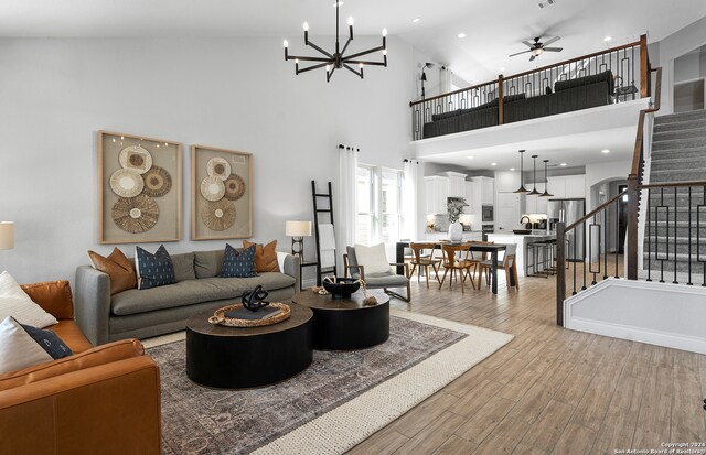 living room with sink, high vaulted ceiling, ceiling fan with notable chandelier, and light wood-type flooring