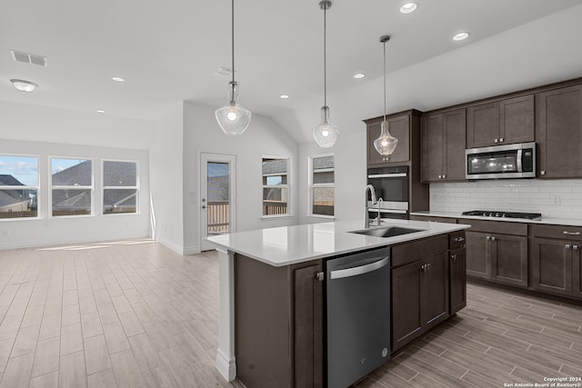 kitchen with stainless steel appliances, sink, pendant lighting, and a center island with sink