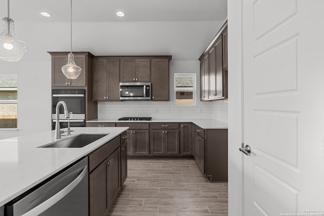 kitchen featuring backsplash, sink, decorative light fixtures, appliances with stainless steel finishes, and light hardwood / wood-style floors