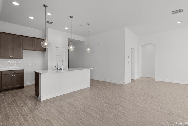 kitchen with light hardwood / wood-style flooring, dark brown cabinetry, decorative light fixtures, and an island with sink