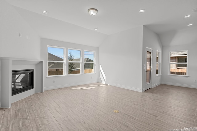 unfurnished living room featuring vaulted ceiling, a wealth of natural light, and light wood-type flooring