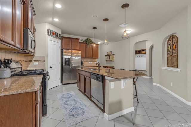 kitchen with an island with sink, hanging light fixtures, sink, appliances with stainless steel finishes, and tasteful backsplash