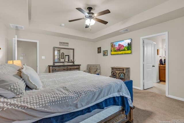 bedroom with ceiling fan, ensuite bath, a tray ceiling, and light colored carpet