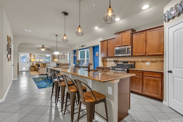 kitchen featuring appliances with stainless steel finishes, sink, hanging light fixtures, ceiling fan, and a kitchen island with sink