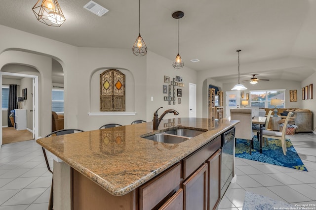 kitchen featuring sink, decorative light fixtures, light stone counters, light tile patterned floors, and a kitchen island with sink