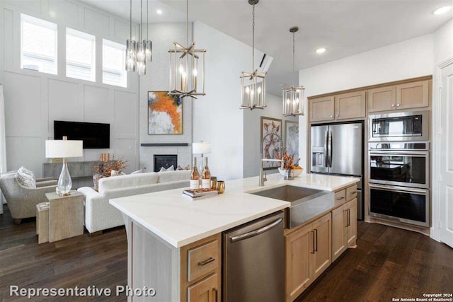 kitchen with a center island with sink, a fireplace, stainless steel appliances, and hanging light fixtures