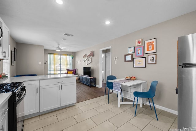 kitchen with stainless steel fridge, white cabinets, ceiling fan, light wood-type flooring, and gas range