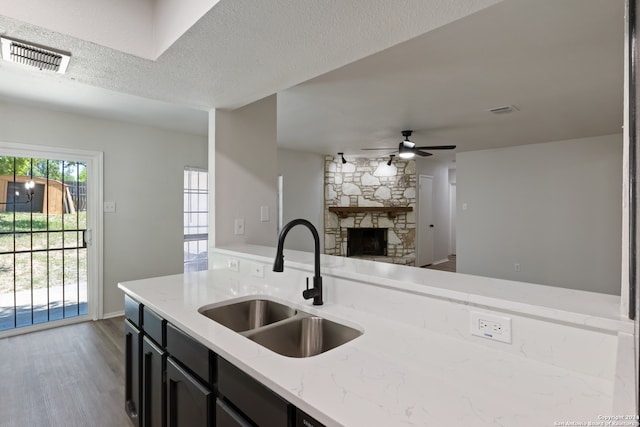 kitchen with sink, a fireplace, a textured ceiling, hardwood / wood-style floors, and light stone counters