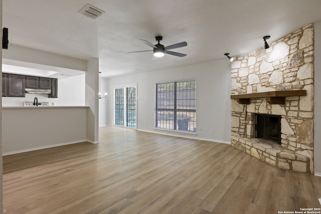 unfurnished living room featuring light hardwood / wood-style floors, a textured ceiling, a stone fireplace, and ceiling fan with notable chandelier