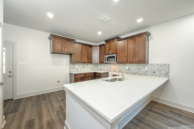 kitchen with kitchen peninsula, backsplash, dark wood-type flooring, and sink