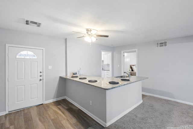 kitchen featuring hardwood / wood-style flooring, kitchen peninsula, sink, light stone counters, and ceiling fan