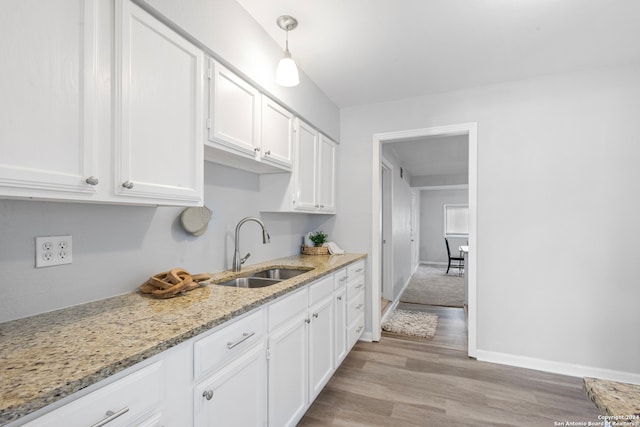 kitchen featuring sink, white cabinetry, light hardwood / wood-style floors, pendant lighting, and light stone counters