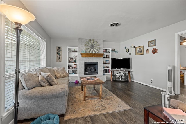 living room with dark wood-type flooring, built in features, and a large fireplace