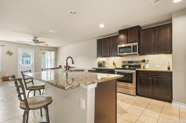 kitchen with dark brown cabinets, stainless steel appliances, backsplash, a center island with sink, and sink