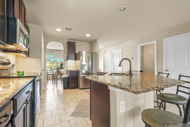 kitchen with appliances with stainless steel finishes, sink, an island with sink, a kitchen bar, and backsplash