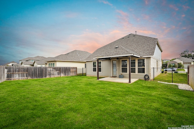 back house at dusk featuring a yard and a patio area