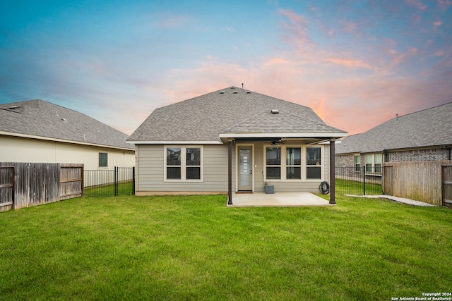 back house at dusk featuring a patio, a lawn, and ceiling fan