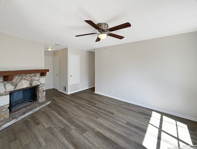 unfurnished living room featuring dark wood-type flooring, a stone fireplace, and ceiling fan