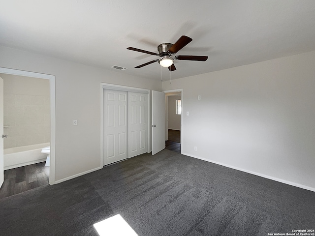 unfurnished bedroom featuring dark carpet, connected bathroom, a closet, and ceiling fan