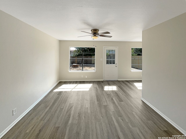 empty room with ceiling fan, a textured ceiling, a wealth of natural light, and dark hardwood / wood-style flooring