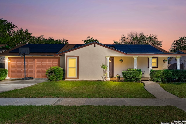 ranch-style house with a yard, solar panels, covered porch, and a garage