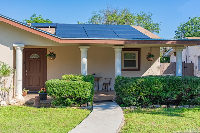 entrance to property featuring a porch, solar panels, and a yard