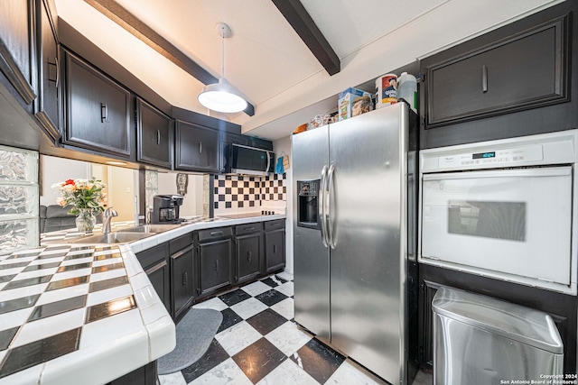 kitchen with appliances with stainless steel finishes, decorative light fixtures, tile counters, beam ceiling, and decorative backsplash