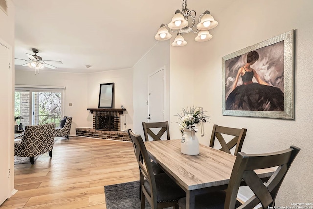 dining room with light hardwood / wood-style floors, ceiling fan with notable chandelier, and a brick fireplace