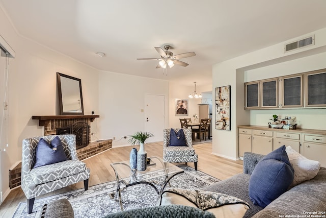 living room with light hardwood / wood-style flooring, a brick fireplace, and ceiling fan with notable chandelier