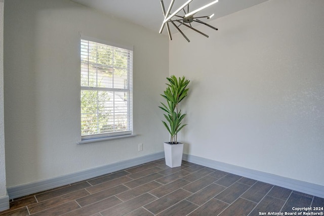 empty room featuring dark wood-type flooring, a wealth of natural light, and a chandelier